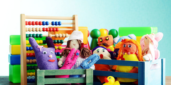 Sprachtherapeutisches Ambulatorium Eine Nahaufnahme verschiedener Spielzeuge in kleinen bunten Holzkisten. Man sieht Stoffpuppen, eine Gummiente, Spielfiguren und einen Abakus mit bunten Holzperlen.